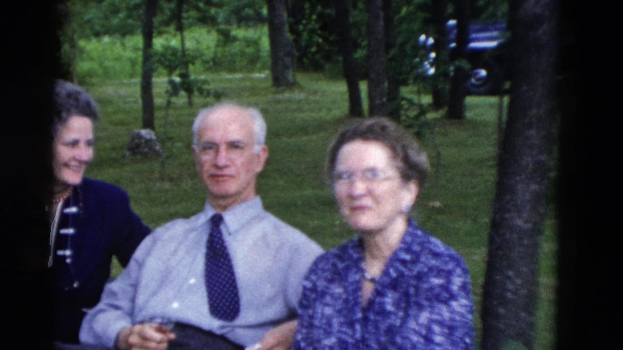 In 1975 Somerset, Kentucky home-movie footage, three adults sit outdoors on a green wooded lawn during a backyard gathering.