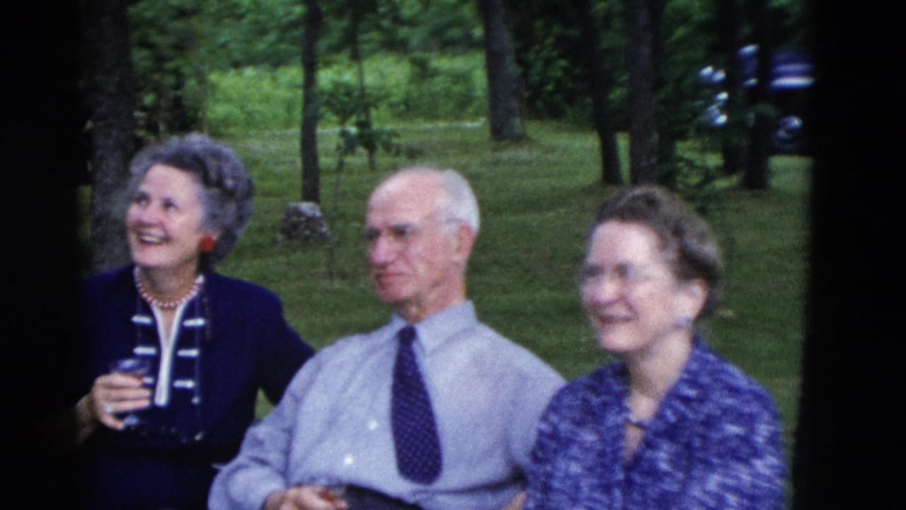 Two women and an older man sit outdoors, one woman smiling while holding a glass.