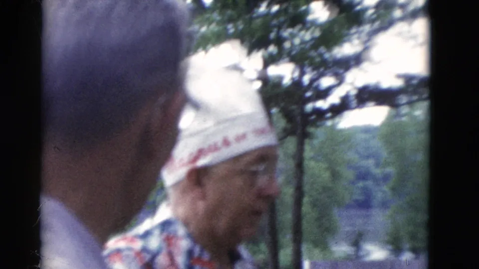 1975 Somerset, Kentucky 8mm frame of two older men talking outdoors, one in a white embroidered hat and patterned shirt.