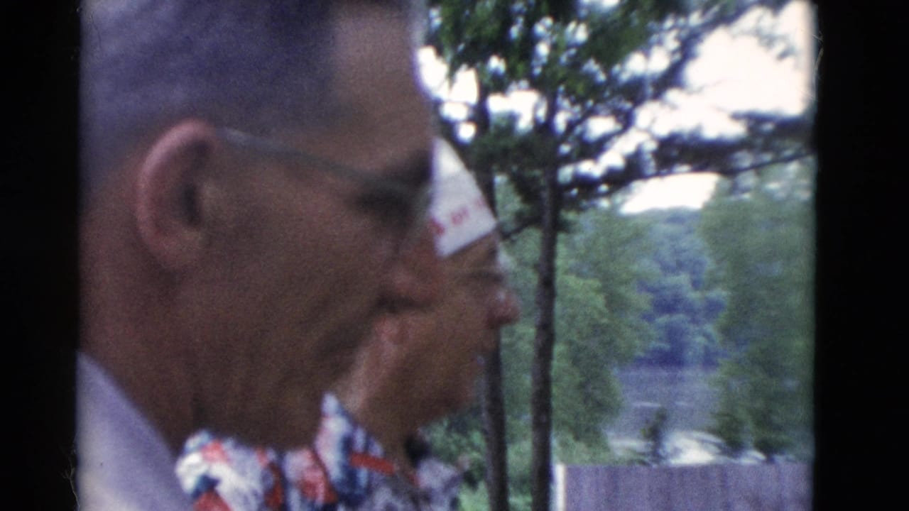 Close 8mm view of an older man with glasses beside a hat-wearing man at a wooded Somerset, Kentucky setting in 1975.