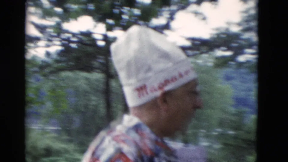 1975 home-movie frame from Somerset, Kentucky showing an older man in a white embroidered hat walking or turning near trees.