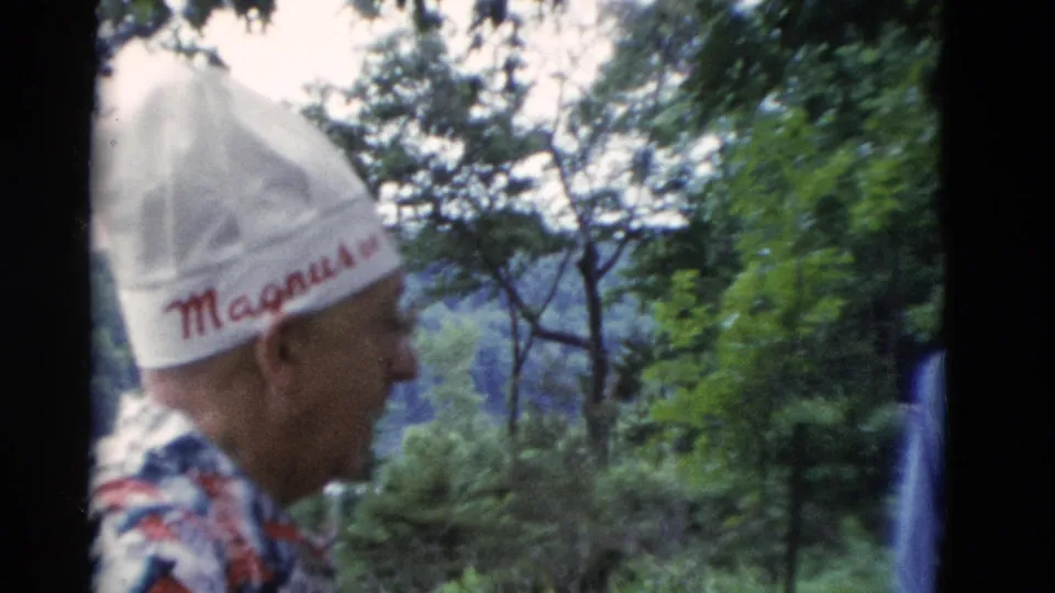 Somerset, Kentucky 1975 8mm frame of an older man in an embroidered white hat near trees with water or hills in the background.