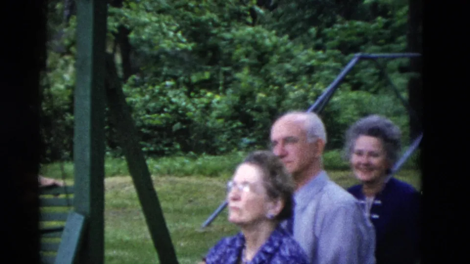 1975 Somerset, Kentucky frame with older adults gathered near green swing-set supports in a leafy backyard.