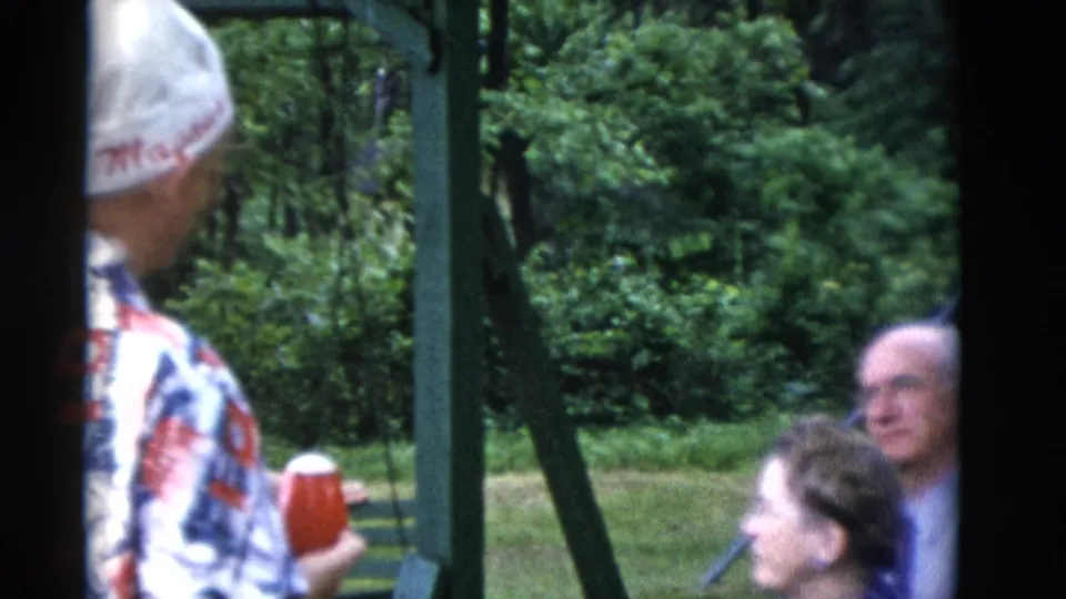 1975 Somerset, Kentucky frame with a man in a white hat holding a red cup as older adults stand in the backyard.