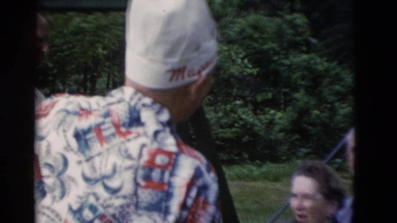 Man in white cap and patterned shirt turns toward older adults in a green outdoor Somerset, Kentucky setting.