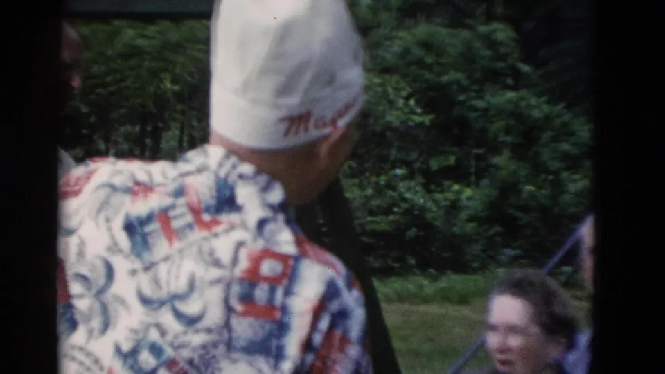 Man in white cap and patterned shirt turns toward older adults in a green outdoor Somerset, Kentucky setting.