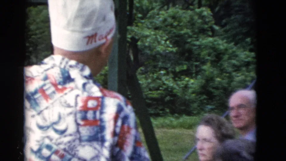 1975 Somerset, Kentucky frame with a man in a white cap near seated older adults in a wooded outdoor area.