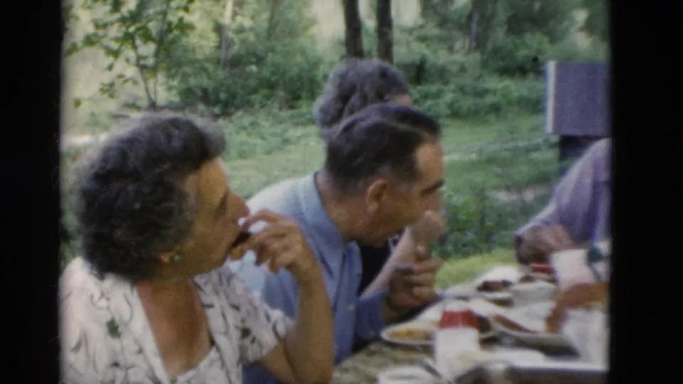1975 Somerset, Kentucky frame of older adults at an outdoor picnic table, with a woman holding a cigarette during the meal.