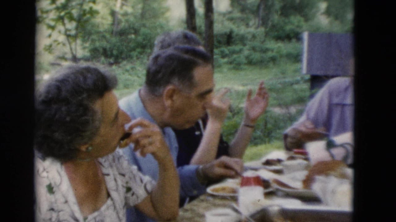 Older men and women in 1975 Somerset, Kentucky home-movie footage sit around an outdoor table while eating and talking.