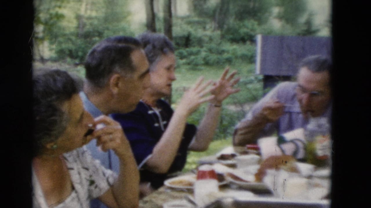 Several older adults sit at a table as one person gestures with both hands.