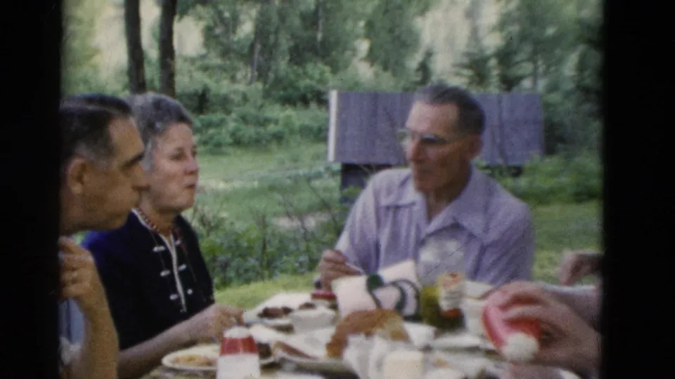 Older adults in 1975 Somerset, Kentucky footage sit at a wooded outdoor table with food, cups, and casual conversation.