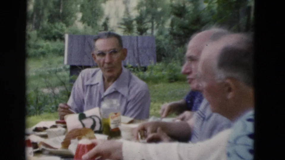 Older adults at an outdoor picnic table in Somerset, Kentucky, in 1975, with food, cups and trees behind them.