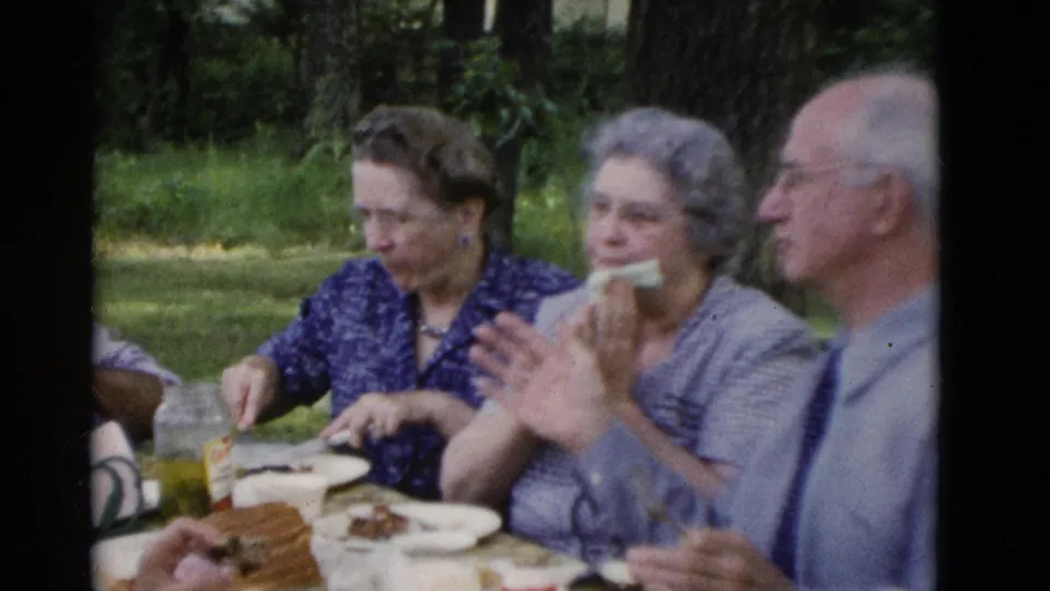 Older adults continue eating at an outdoor picnic table in Somerset, Kentucky, with soft 8mm color and visible tableware.