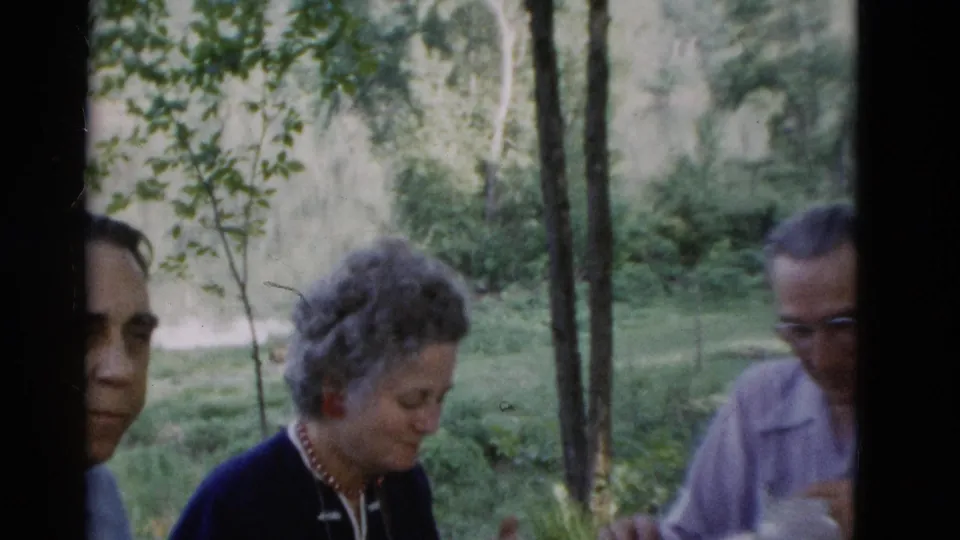 Three older adults are partly framed at a wooded outdoor gathering in 1975 Somerset, Kentucky footage.