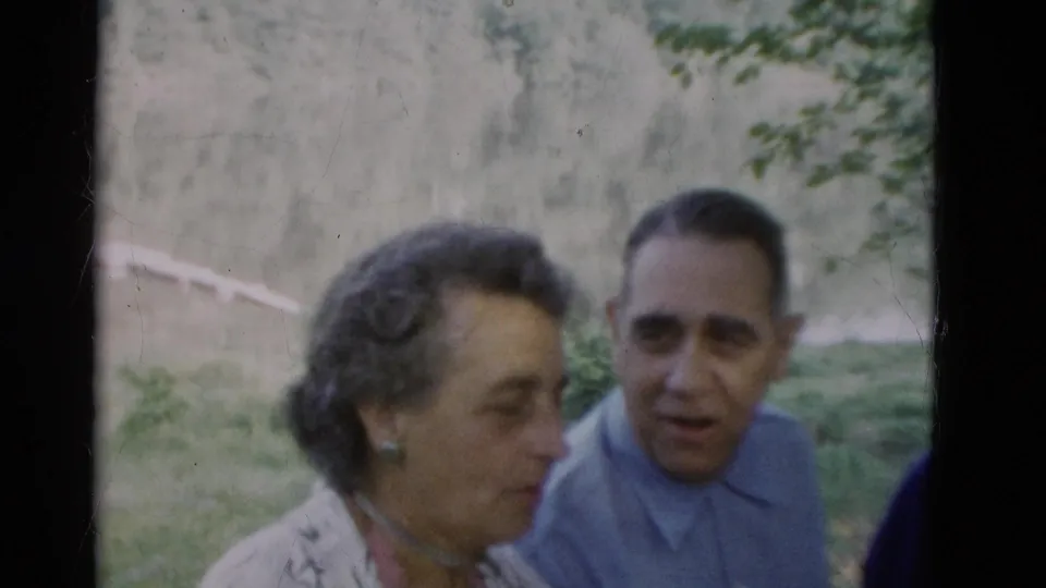 Final 8mm frame shows an older woman passing foreground while an older man looks ahead in a wooded Somerset, Kentucky setting.