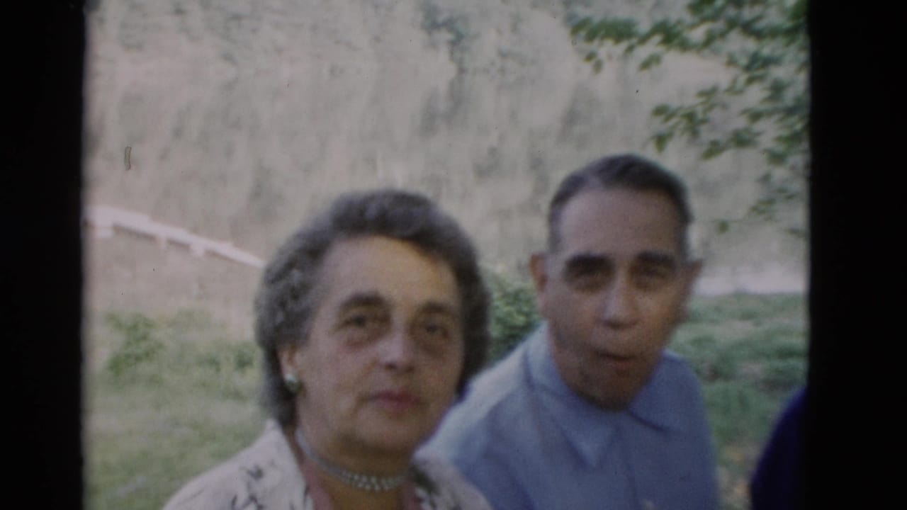 Older woman and older man seated outdoors, looking toward the camera in a grassy area.