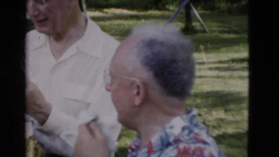 1975 Somerset, Kentucky 8mm frame with two older men conversing outdoors, one smiling in a white shirt and another turned partly away.