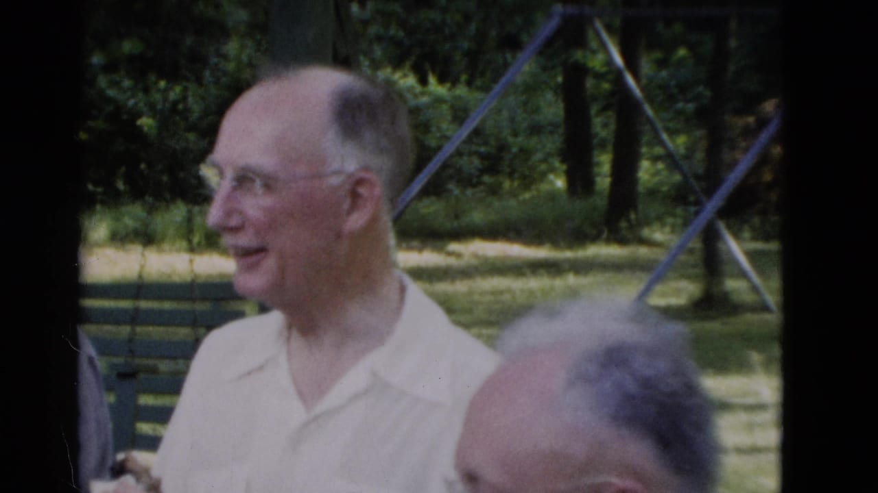 An older man in glasses and a light collared shirt smiles during a 1975 Somerset, Kentucky park gathering, with another man's head in the foreground.
