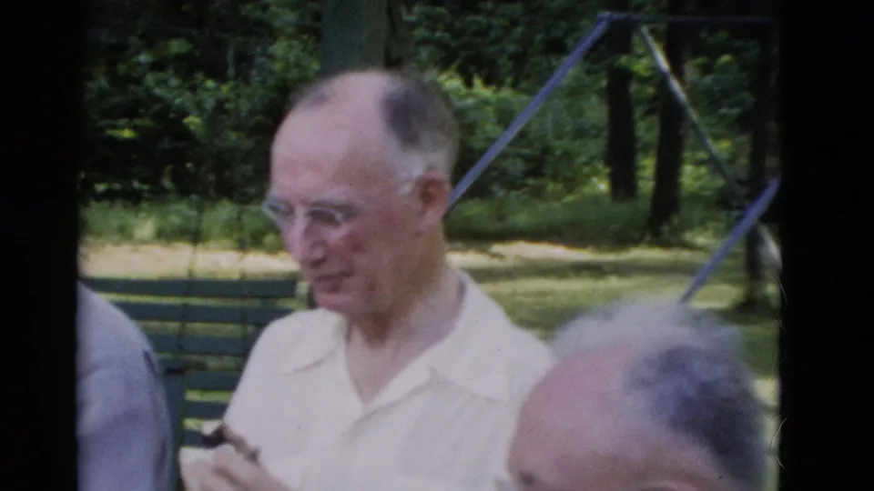 In the 1975 Somerset park footage, an older man in glasses looks down while a patterned-shirt man and another seated figure are partly visible.