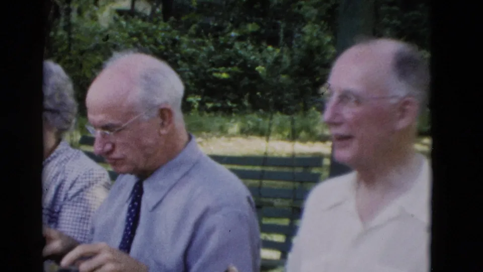 Older men sit on a green park bench in 1975 Somerset, Kentucky footage, with one man in a shirt and tie handling a small object.