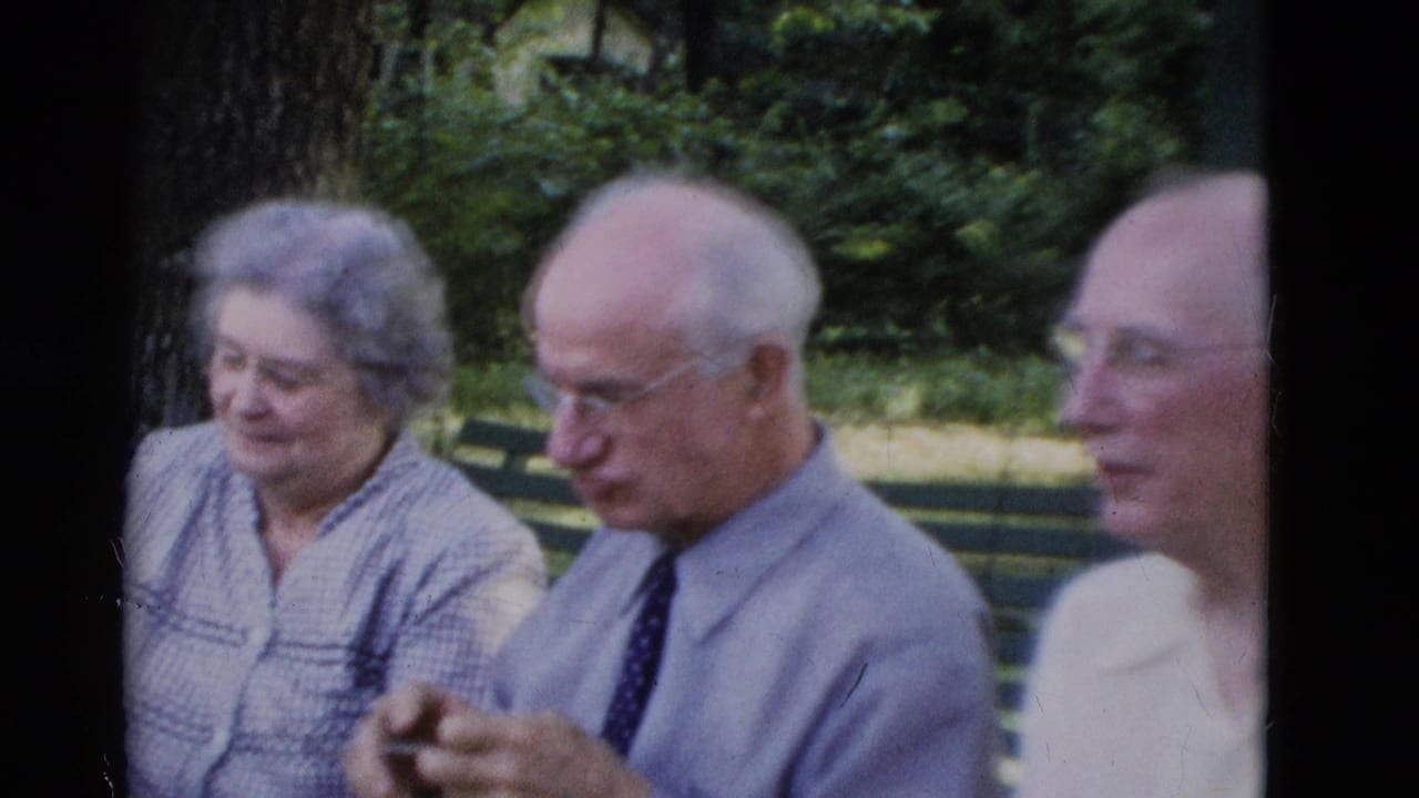 Older adults sit on a green park bench in Somerset, Kentucky, in 1975 home-movie footage, with trees and lawn behind them.