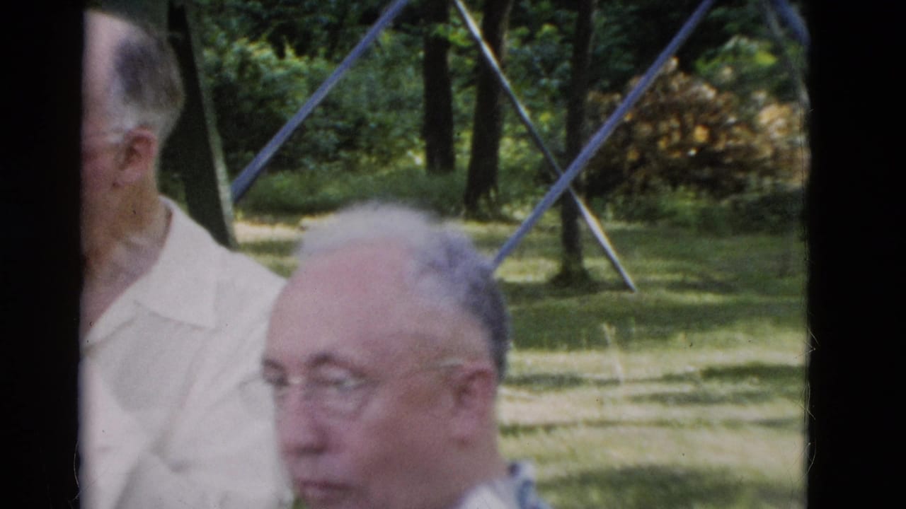 Two older men in light shirts near a park bench and metal frame outdoors.
