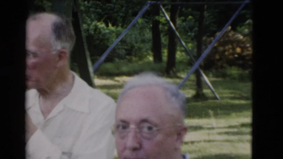A close, partly cropped 1975 home-movie frame shows older men near a green park bench in Somerset, Kentucky, with grass and trees behind them.