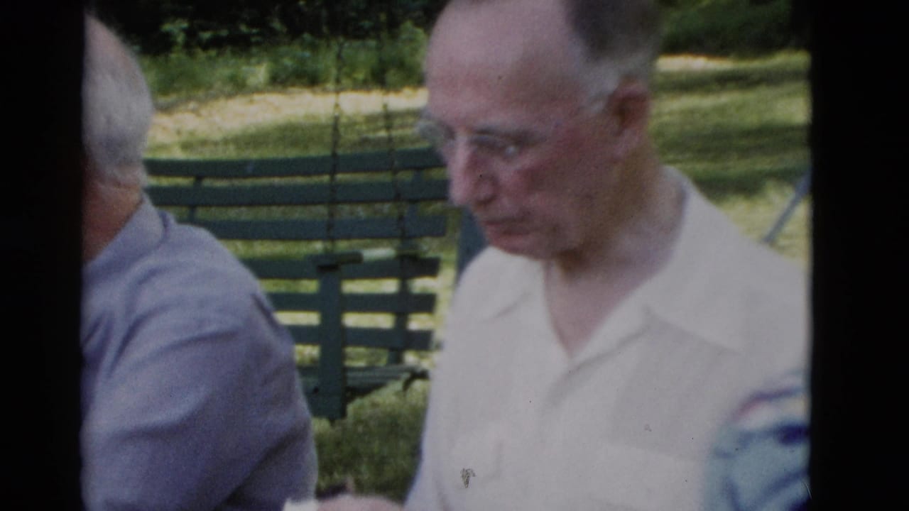 Two elderly men seated at an outdoor park bench, one in a white collared shirt facing forward.