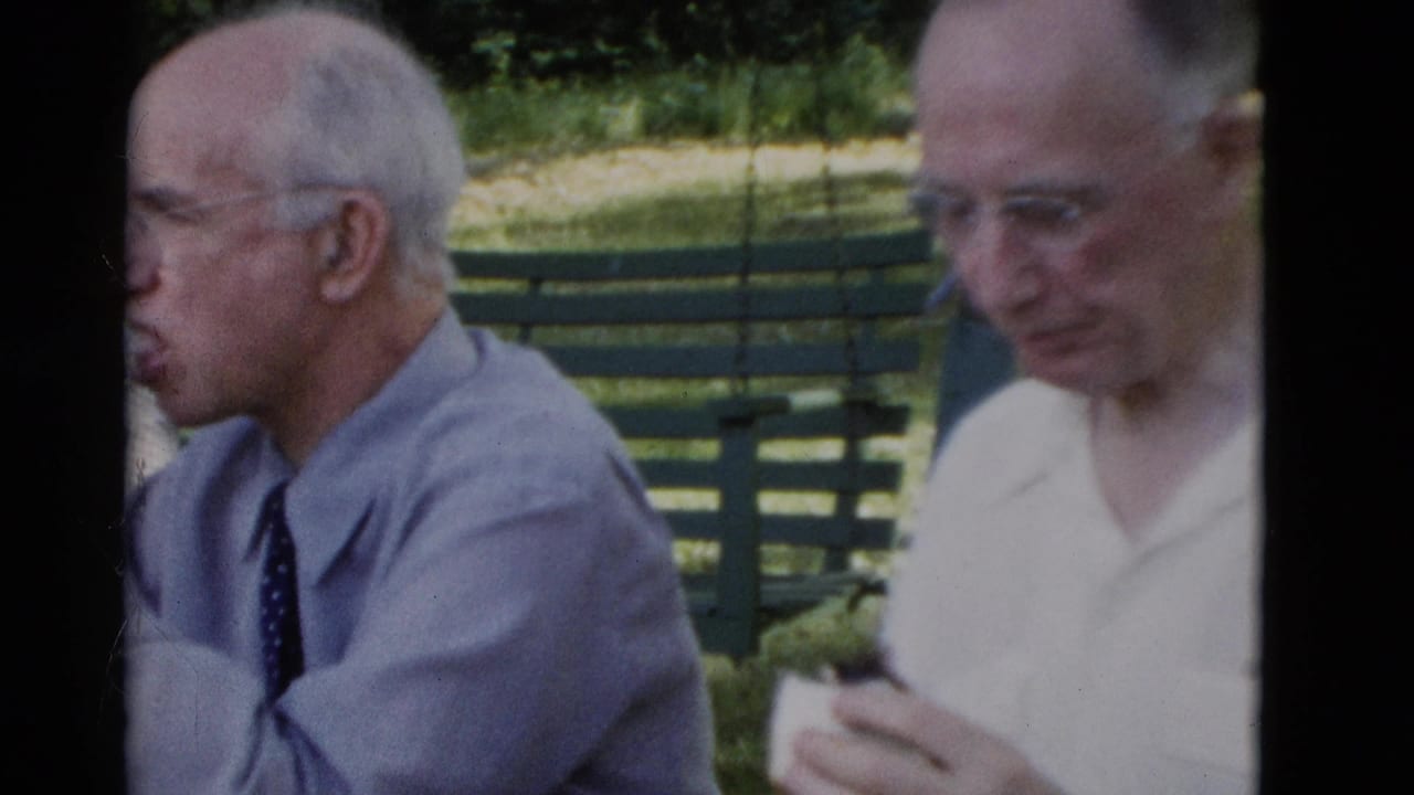1975 Somerset, Kentucky frame showing an elderly man in a blue shirt and tie beside a friend holding food near a park bench.