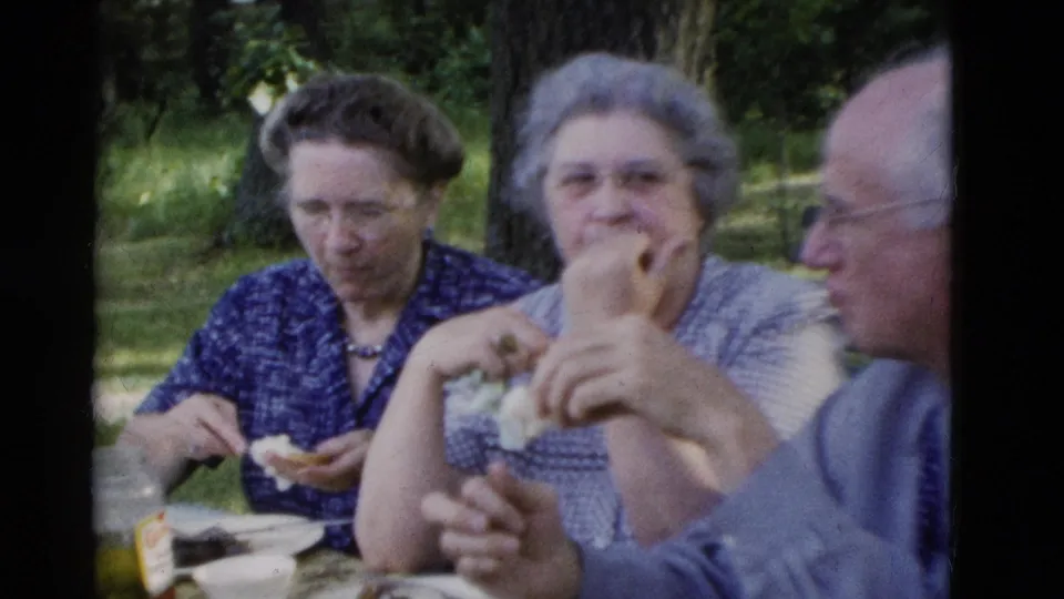 1975 8mm frame from Somerset, Kentucky showing older adults seated at a park table, eating in an informal home-movie moment.