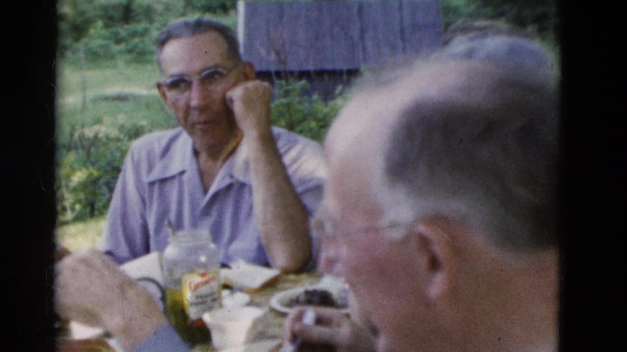 Man in a light purple shirt sits at a picnic table near a condiment jar.