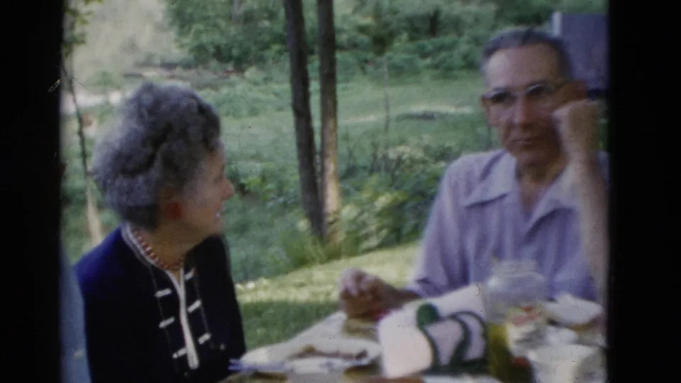 A woman in a dark jacket and red earrings turns toward a man at the 1975 Somerset outdoor picnic table.