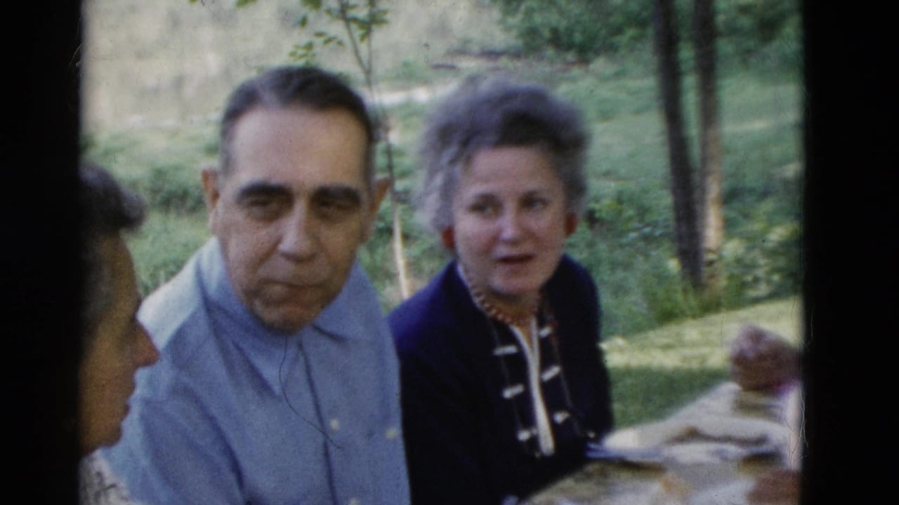 1975 Somerset, Kentucky home-movie frame showing an older man in a light blue shirt beside a woman in a dark jacket at an outdoor table.