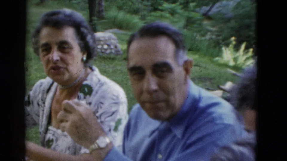 1975 Somerset, Kentucky home-movie frame of an older woman gesturing while seated beside an older man at an outdoor table.