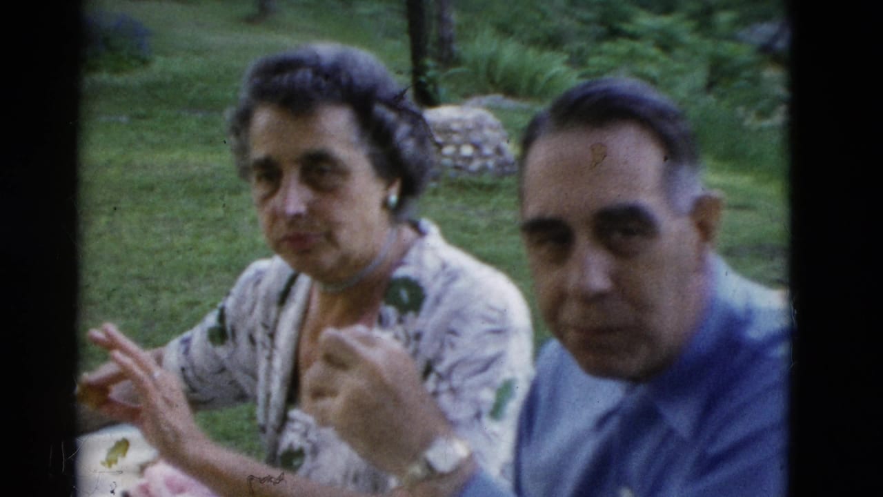 In the 1975 Somerset, Kentucky home-movie scene, a woman gestures with food in hand while a man in a blue shirt sits beside her at the table.