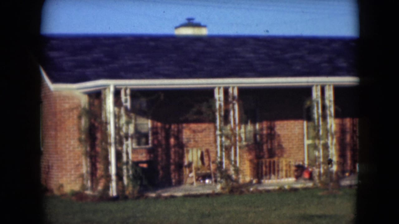 Brick house with a covered porch, white columns, lawn, and blue sky.