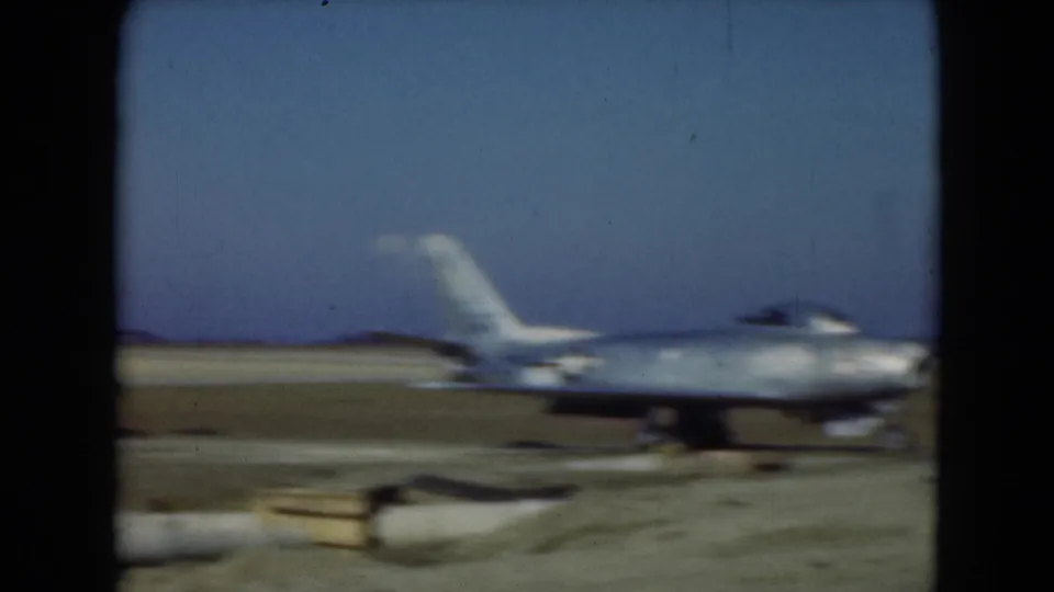 1975 Middletown, Pennsylvania home-movie frame showing a parked silver jet on an airfield with soft motion blur.
