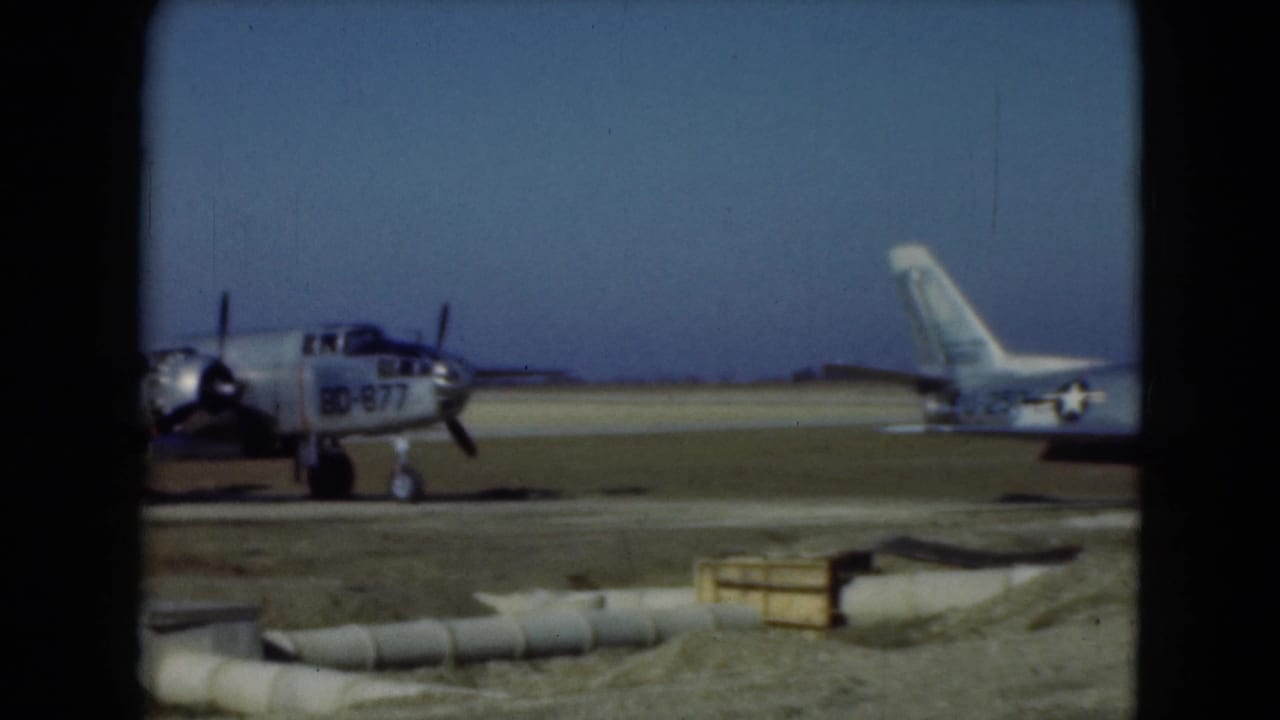 1975 Middletown, Pennsylvania 8mm frame showing a propeller aircraft marked BD-877 near a parked jet on a sunny airfield.