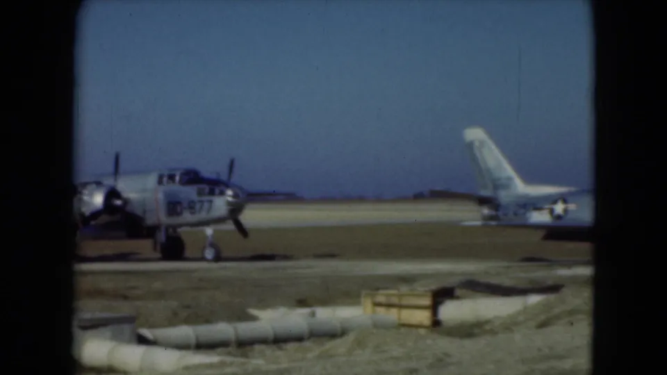 1975 Middletown, Pennsylvania 8mm frame showing a propeller aircraft marked BD-877 near a parked jet on a sunny airfield.