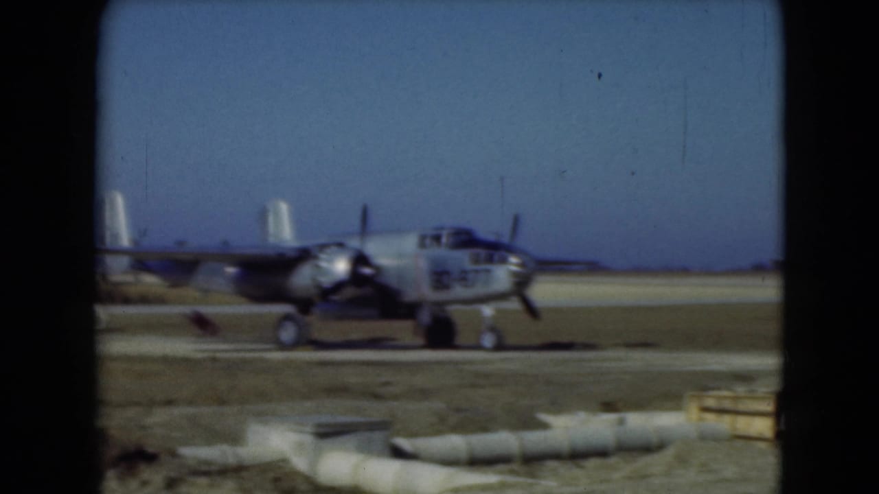 1975 Middletown, Pennsylvania 8mm frame of a propeller aircraft moving across an open airfield with equipment and barriers in view.