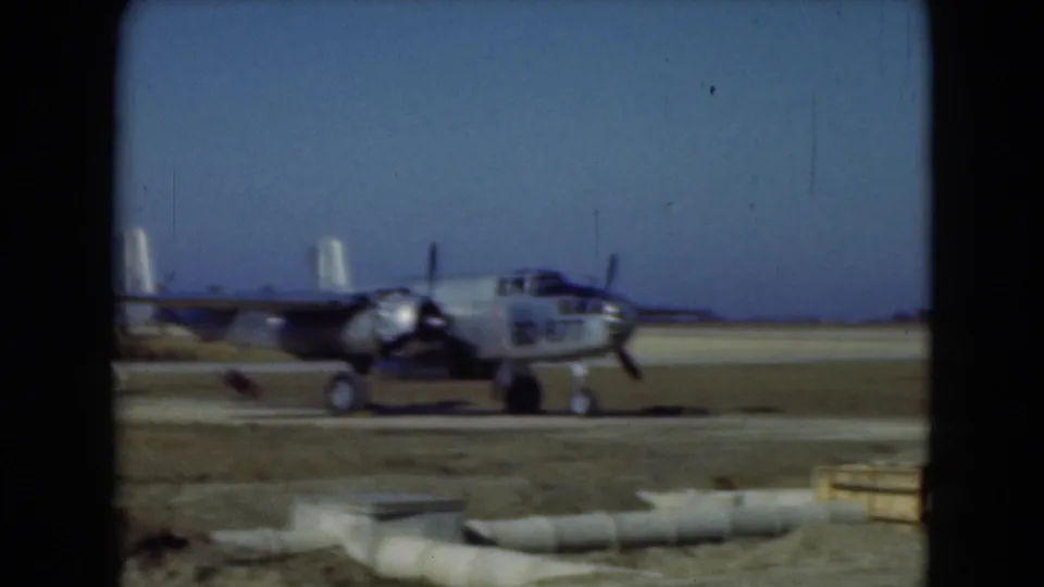 1975 Middletown, Pennsylvania 8mm frame of a propeller aircraft moving across an open airfield with equipment and barriers in view.