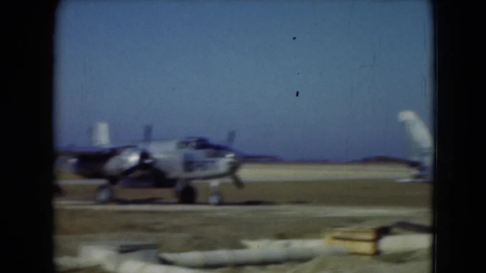 Soft 8mm frame from 1975 Middletown, Pennsylvania showing a propeller aircraft in motion across a sunlit airfield.
