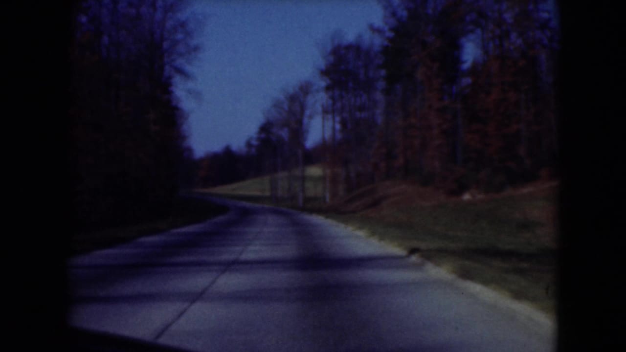1975 Middletown, Pennsylvania 8mm frame of a quiet paved road curving through leafless trees and grassy roadside.