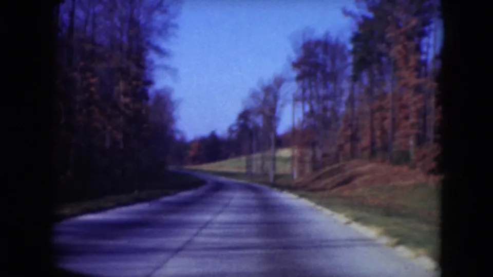 1975 Middletown, Pennsylvania 8mm frame showing a curving road beside bare trees, a grassy bank and blue sky.