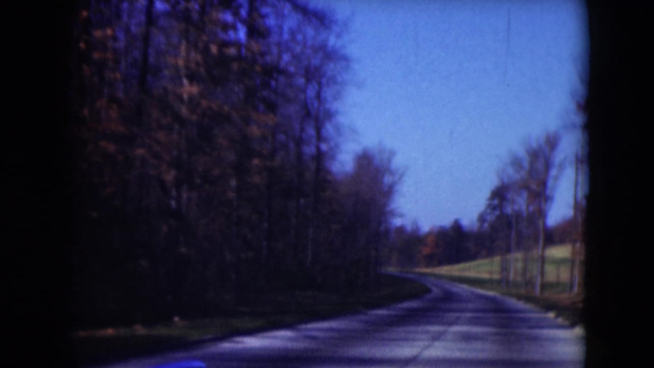 1975 8mm frame from Middletown, Pennsylvania showing a narrow road curving through bare trees and open grass.