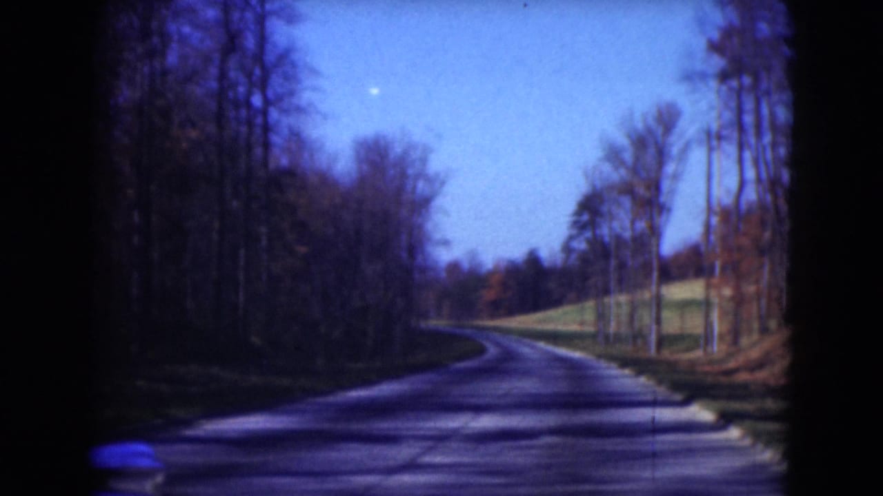 1975 Middletown, Pennsylvania road view with a narrow paved curve, leafless trees, and open grass in saturated 8mm color.