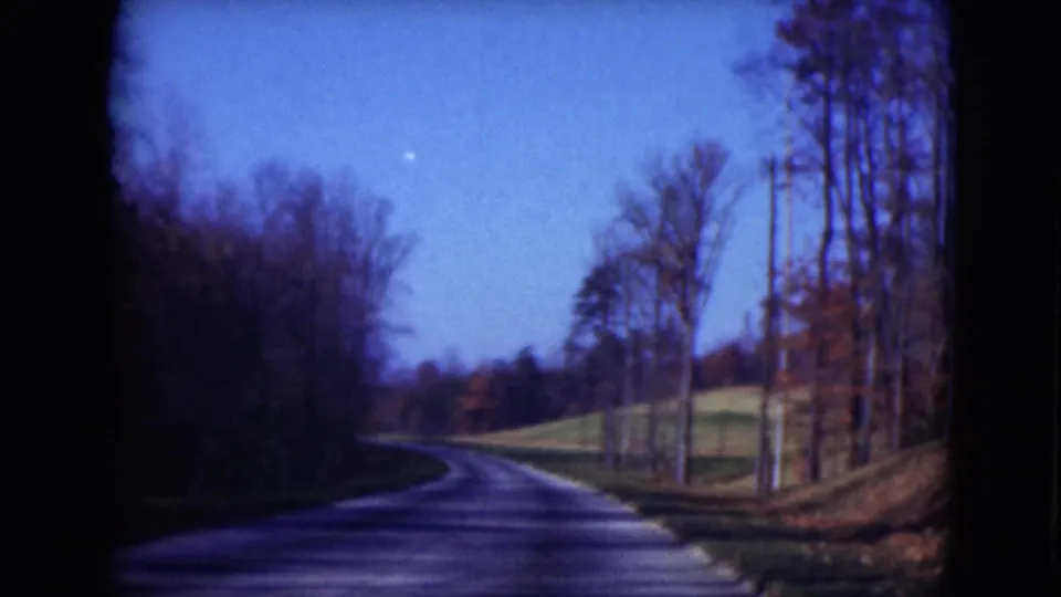 Archival 8mm road view near Middletown, Pennsylvania, with the roadway leading through woods and autumnal roadside color.