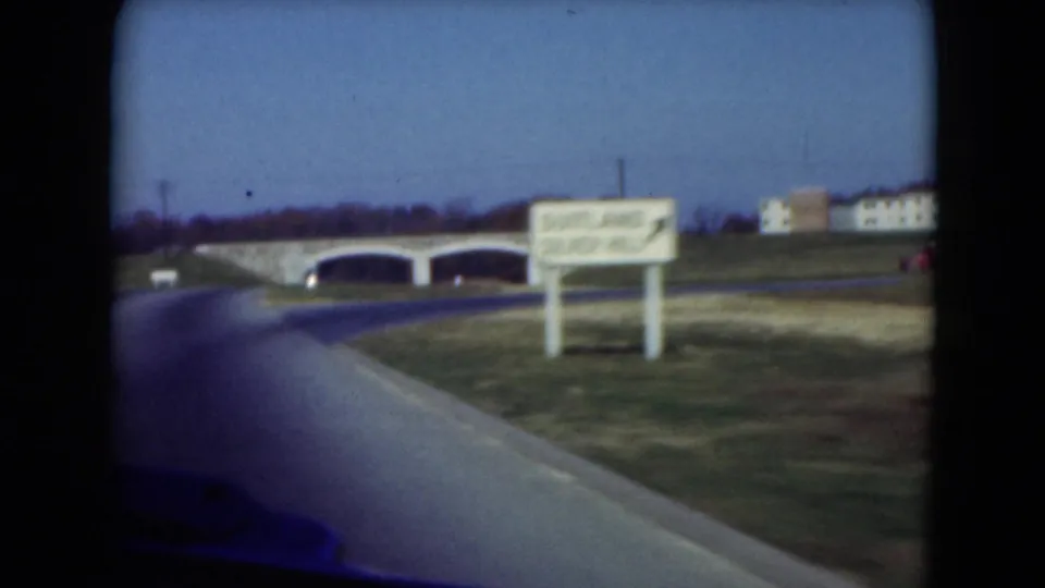 1975 Middletown, Pennsylvania driving frame with a visible dinner hall sign, stone bridge, road edge and distant buildings.