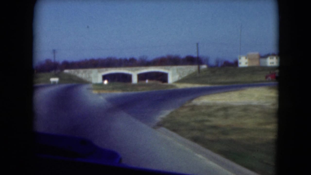 1975 Middletown, Pennsylvania road view from inside a moving vehicle approaching a stone bridge with two arches and grassy embankments.