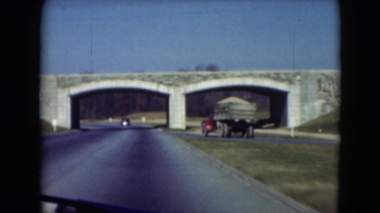 Roadway approaching a stone arch bridge with a truck near the right arch.